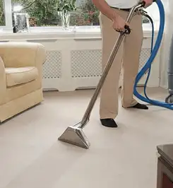 Professional carpet cleaner using a hot-water extraction wand and hose machine in a living room in Omaha, NE.