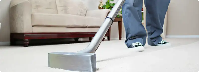 Carpet cleaning technician using a hot-water extraction wand on a light-colored carpet in a living room, Omaha, NE.