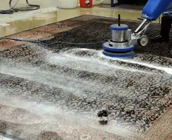Professional rug cleaning with a rotary floor machine and shampoo foam, deep-cleaning an area rug, in Omaha, NE.