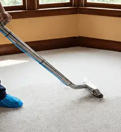 Steam carpet cleaning technician using a hot-water extraction wand on a residential carpet, wearing blue protective shoe covers Omaha, NE.