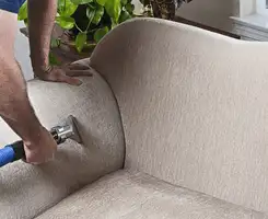 Professional upholstery cleaner deep-cleaning a fabric sofa with a handheld extraction tool and hose in Omaha, NE.